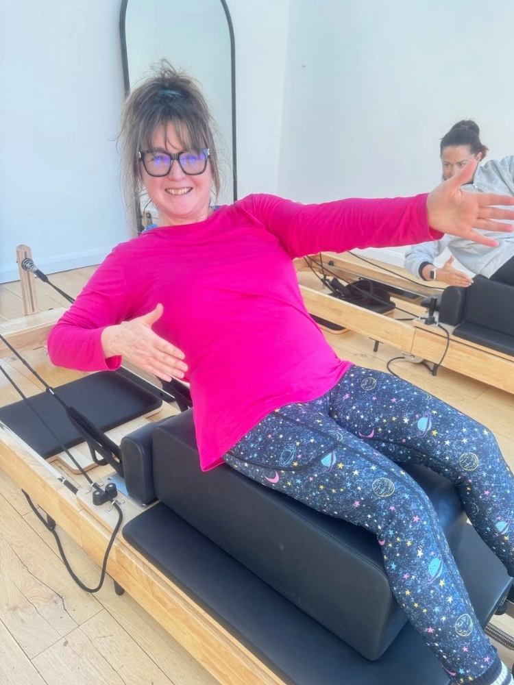 Two women performing reformer Pilates exercises together in a studio class.