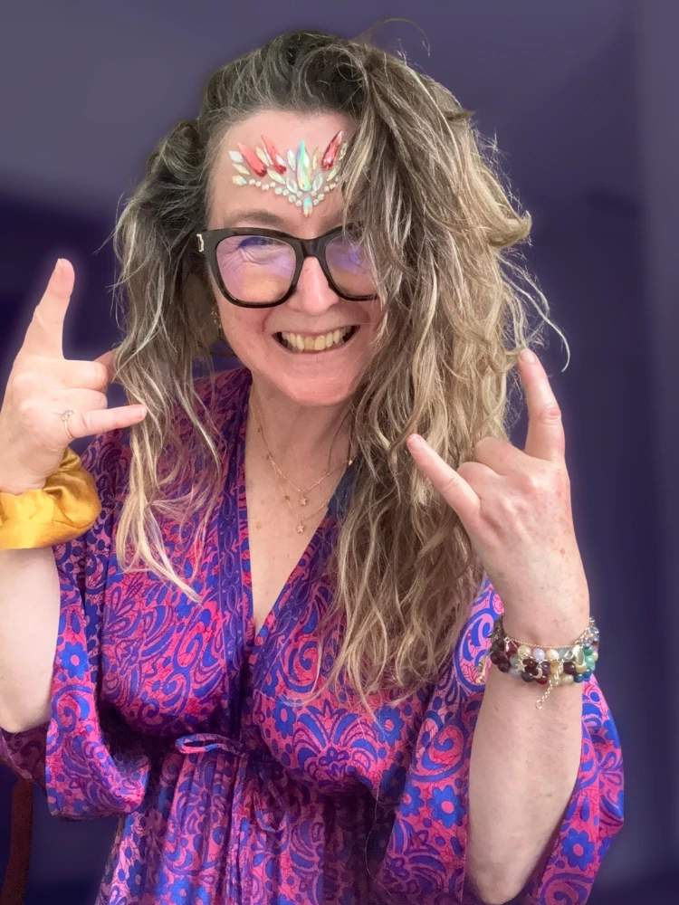 Mairi Taylor smiling and making a joyful gesture, wearing face jewels and a colourful kimono.