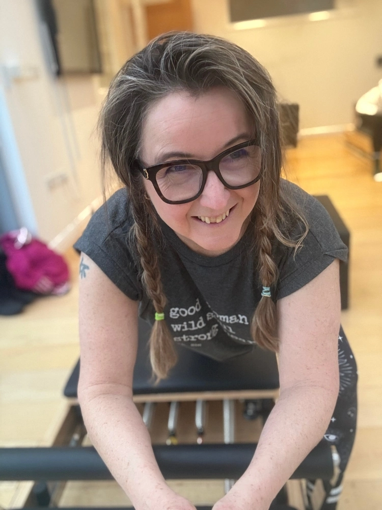 Pilates instructor leaning over a reformer machine in a studio setting.